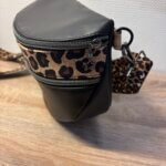 Sac banane en cuir synthétique noir effet satiné. Trois poches zippées. Intérieure toile imperméable. Bandoulière réglable. Vue profil.