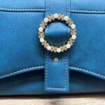 Sac à main femme en cuir écologique. Couleur bleu canard. Format pochette compacte. Porté bandoulière. Boucle décorative.