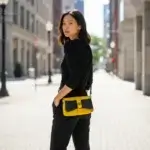 Sac à main femme en liège végétalien. Couleur jaune et empiècement noir motif grainé brillant Format pochette compacte. Porté bandoulière. Porté par mannequin.