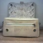 Sac à main femme en liège végétalien. Couleur beige et motifs géométriques. Format pochette compacte. Porté bandoulière. Sac ouvert sur la poche zippèe et les détails du rabat.