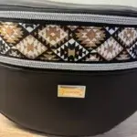 Sac banane en cuir synthétique noir effet satiné. Trois poches zippées. Intérieure toile imperméable. Bandoulière réglable. Détails motif ethnique.