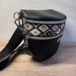 Sac banane en cuir synthétique noir effet satiné. Trois poches zippées. Intérieure toile imperméable. Bandoulière réglable. Vue profil