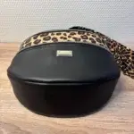 Sac banane en cuir synthétique noir effet satiné. Trois poches zippées. Intérieure toile imperméable. Bandoulière réglable. Vue dessous.
