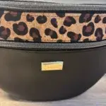 Sac banane en cuir synthétique noir effet satiné. Trois poches zippées. Intérieure toile imperméable. Bandoulière réglable. Vue motif.