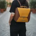 Sac à dos forme carré en cuir écologique marron clair et jaune piqué marron. Vue porté par un mannequin IA